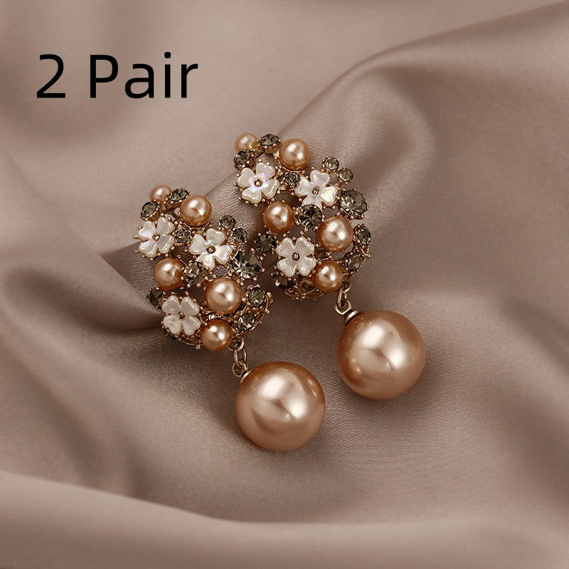 Pair of ornate earrings with pearls and flowers on a beige fabric background