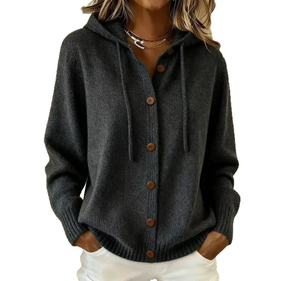 A woman wearing a dark charcoal gray knit cardigan hoodie with brown buttons and drawstrings, paired with white pants, shown against a plain white background.