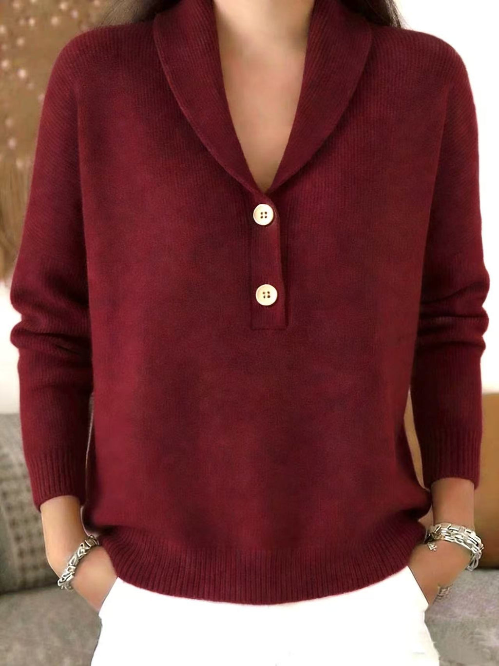 A woman wearing a burgundy knit sweater with a shawl collar and two gold buttons, paired with white pants.