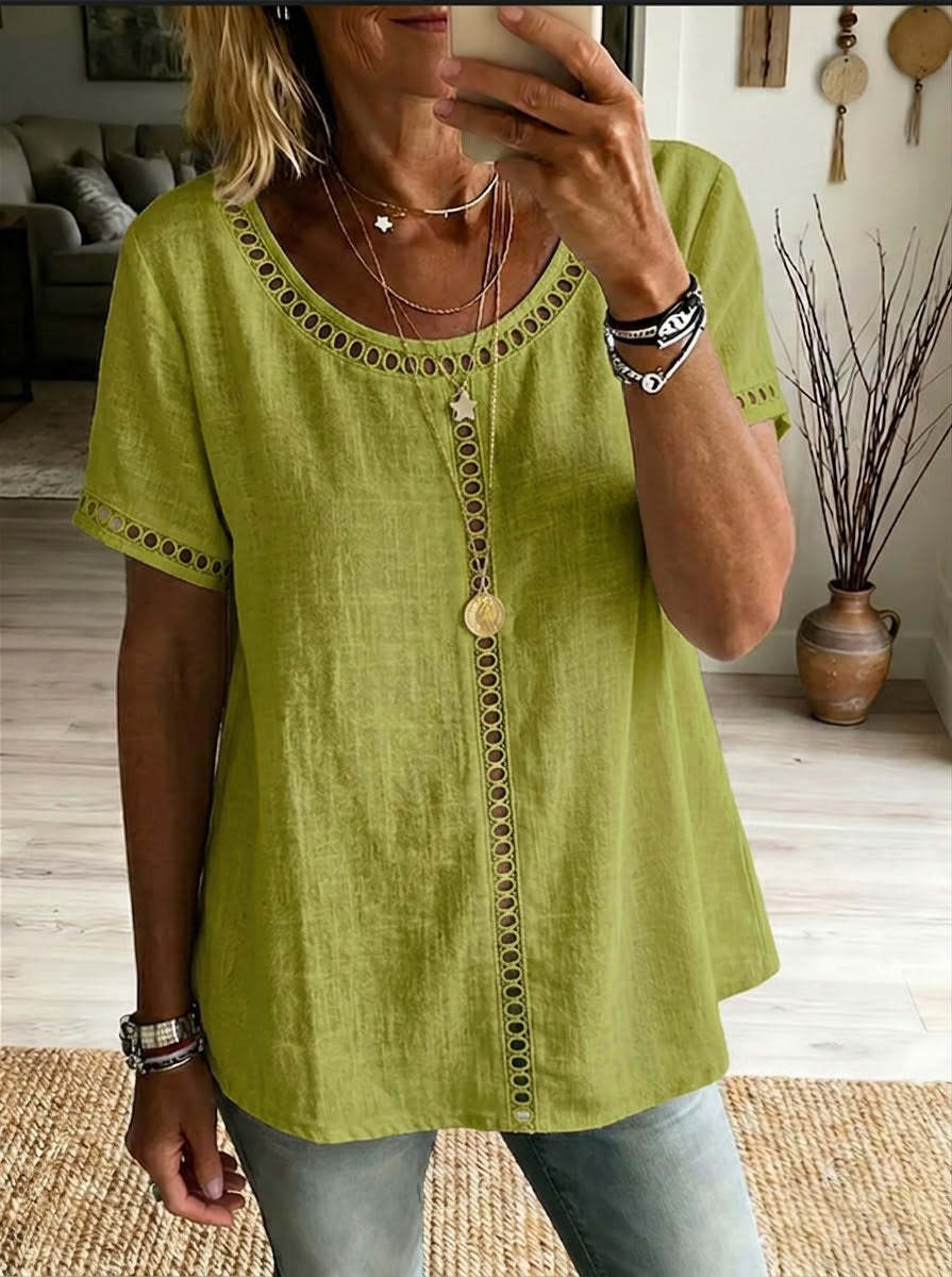 Person wearing a green top with intricate details, standing in a room with a couch and decorative items.
