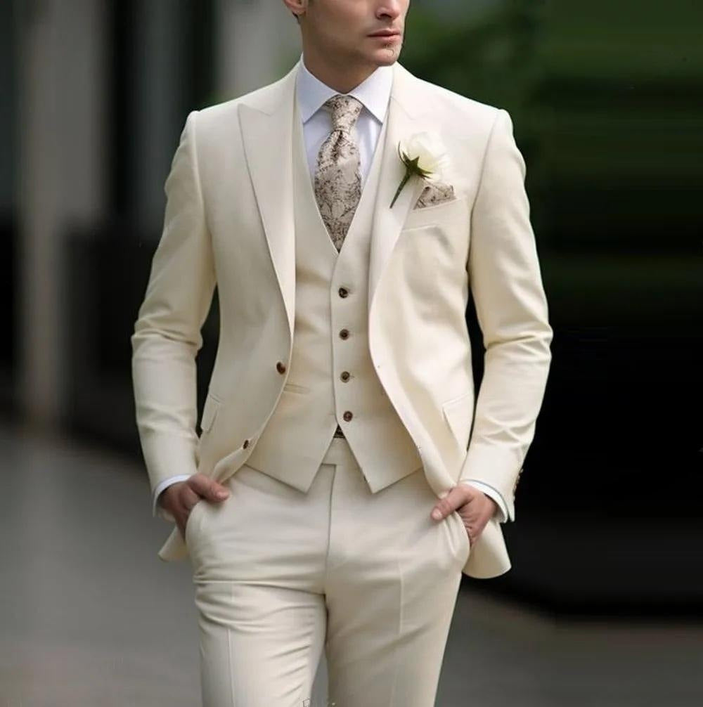 Man wearing a cream suit with a patterned tie and flower, standing against a blurred background.