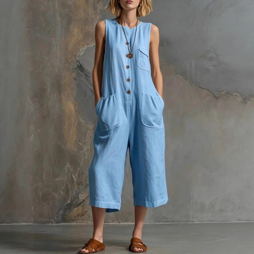 Woman wearing a light blue sleeveless jumpsuit against a textured gray wall.