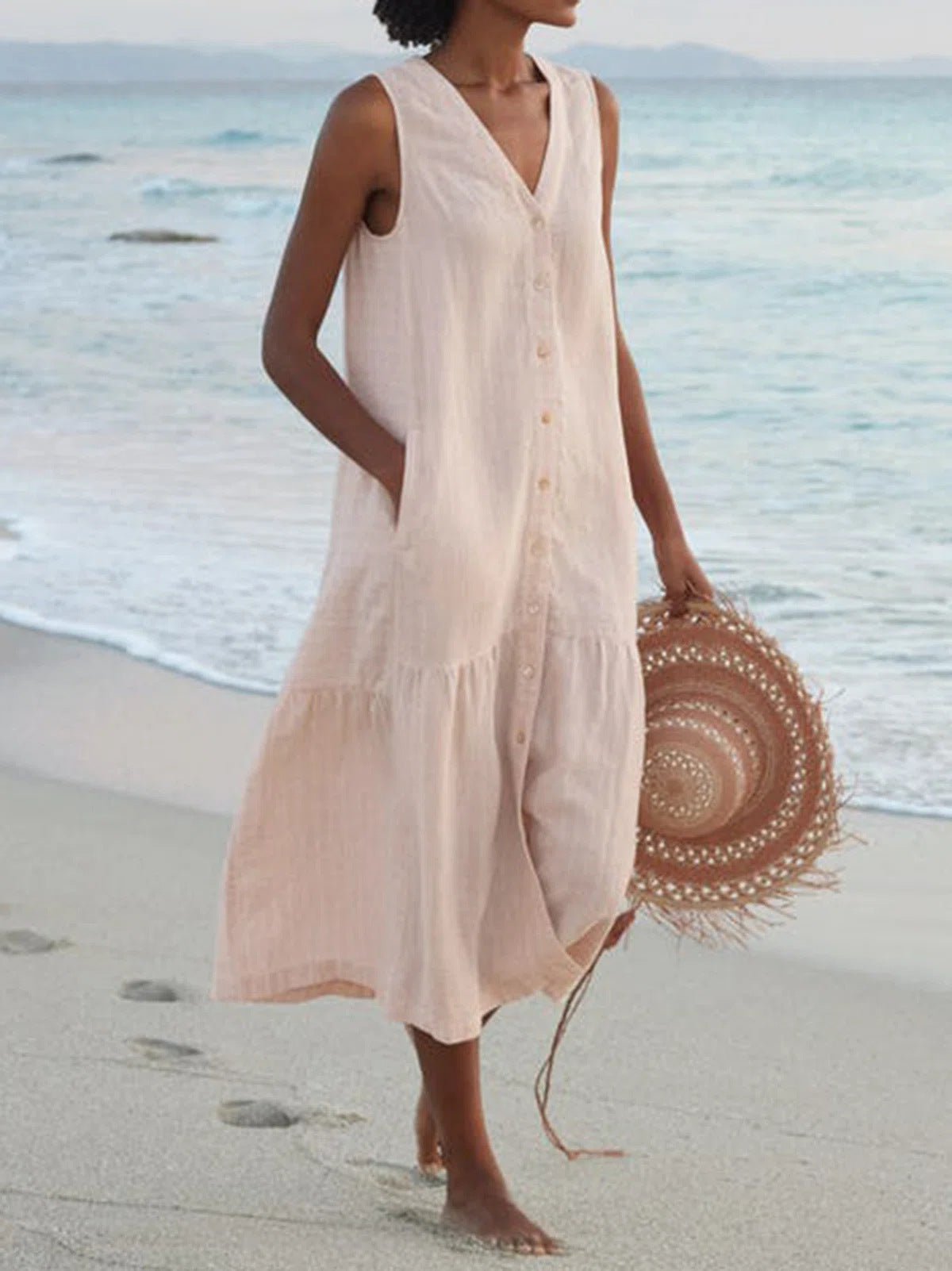Woman in a beige dress holding a straw hat on a beach
