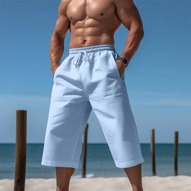 Man wearing light blue shorts on a beach with clear blue sky and ocean.
