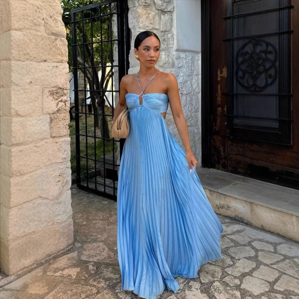 Woman in a blue pleated dress standing in front of a stone building.