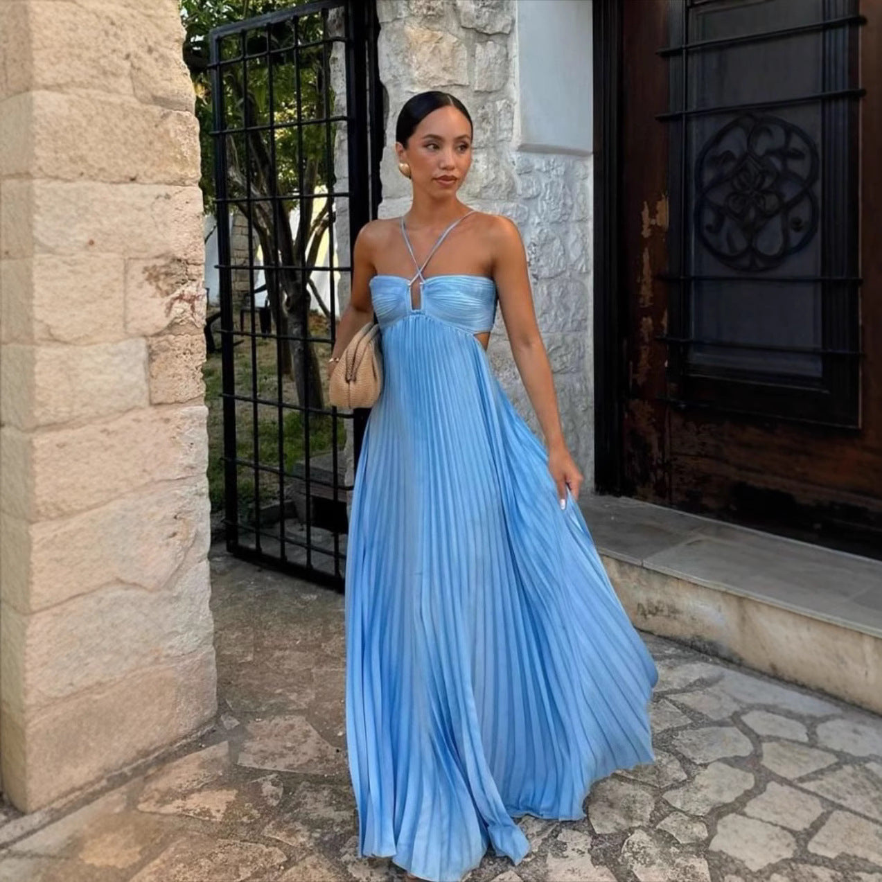 Woman in a blue pleated dress standing in front of a stone building.