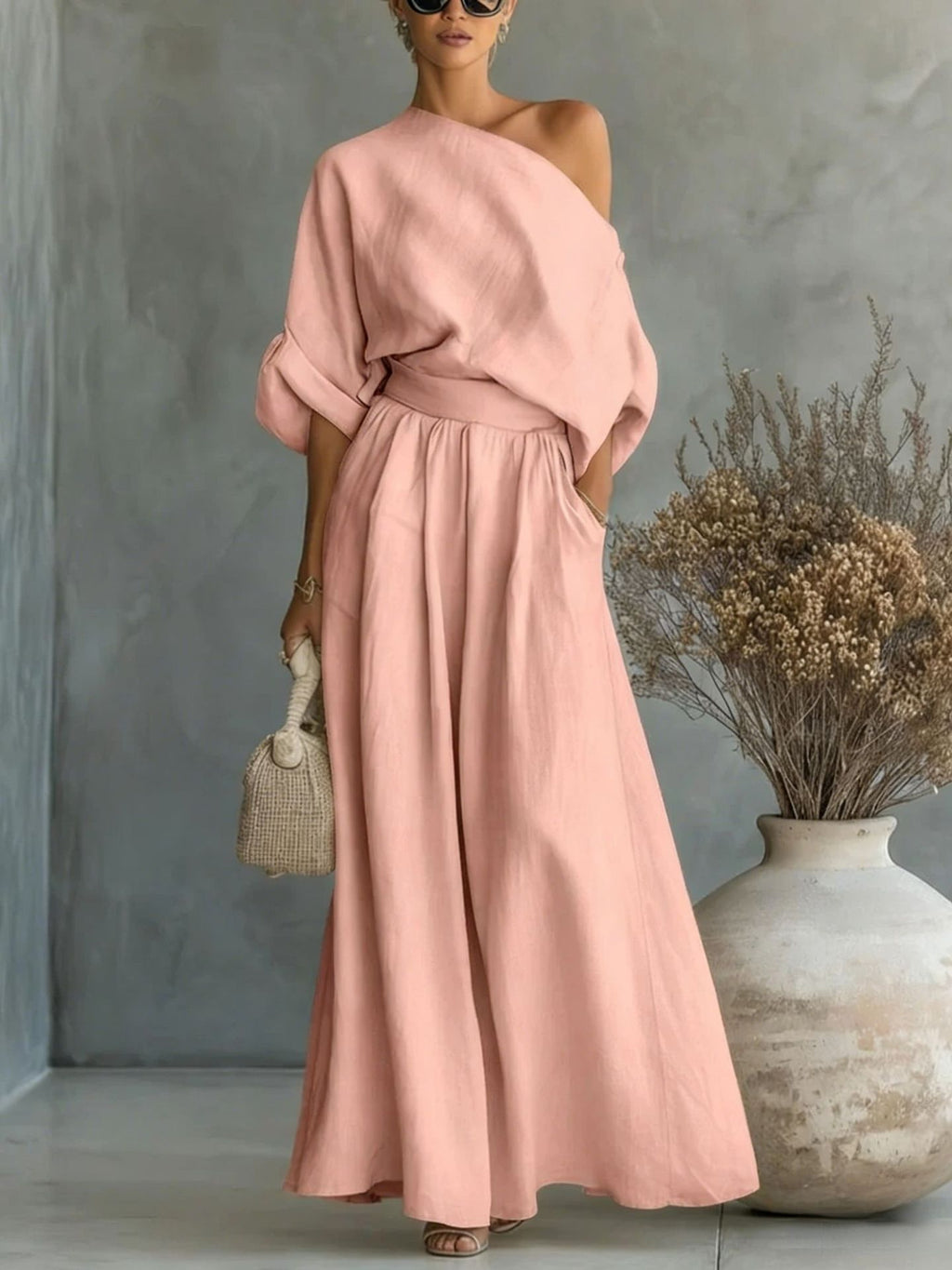 Woman in a pink one-shoulder dress standing next to a textured wall and vase.