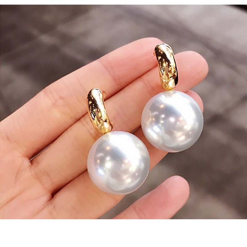 Pearl earrings with gold hooks held in a hand against a blurred background