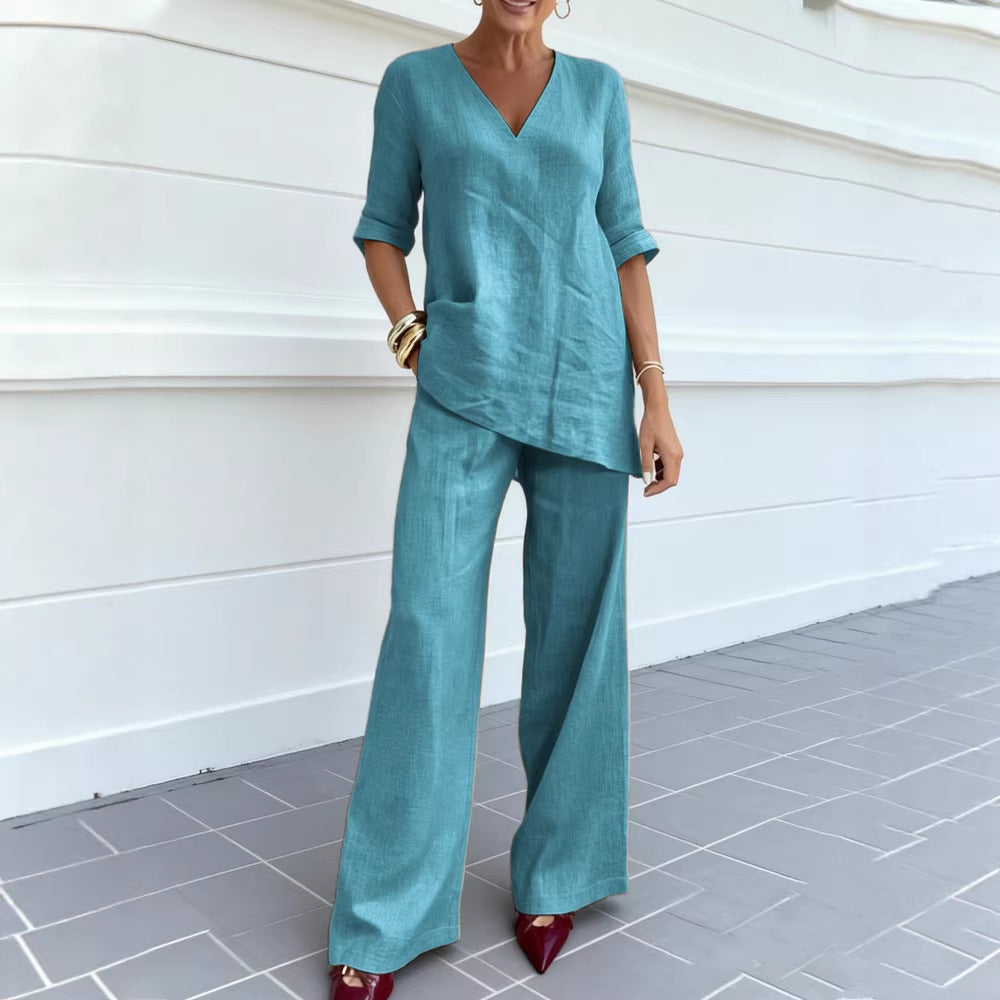 Woman wearing a teal outfit standing against a white wall.