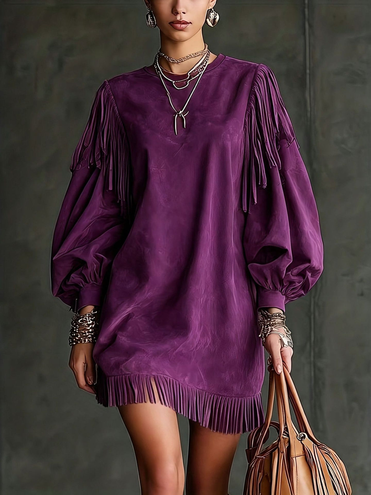 A model wears a purple velvet fringe mini dress with voluminous balloon sleeves, accessorized with layered necklaces, bracelets, and earrings, holding a brown leather fringe handbag against a dark textured studio background.