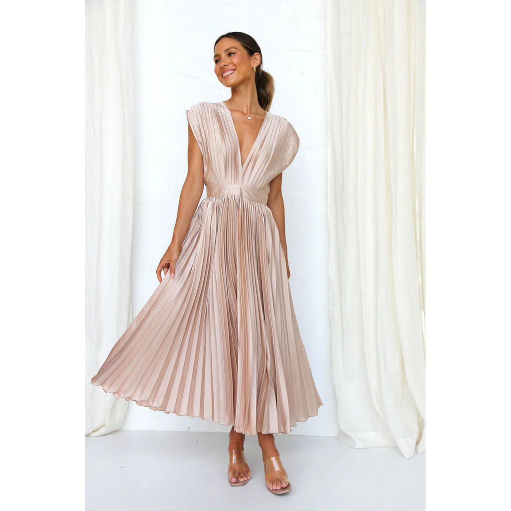 Woman wearing a beige pleated dress against a white curtain background