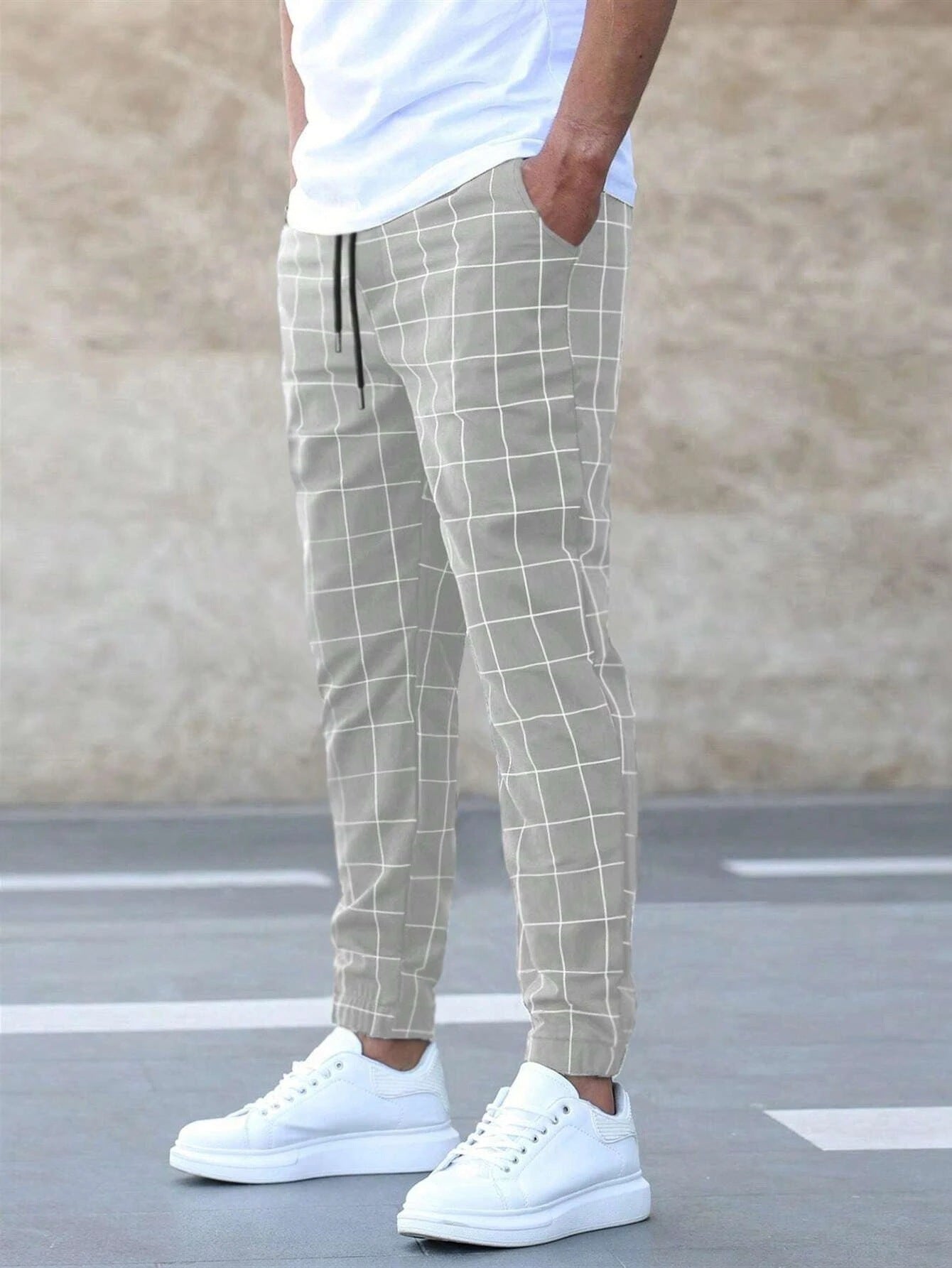Person wearing light gray checkered pants and white sneakers on a street.