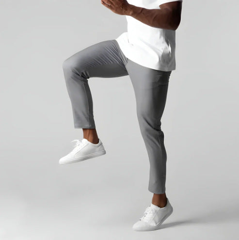 Person wearing gray pants and white sneakers on a plain background