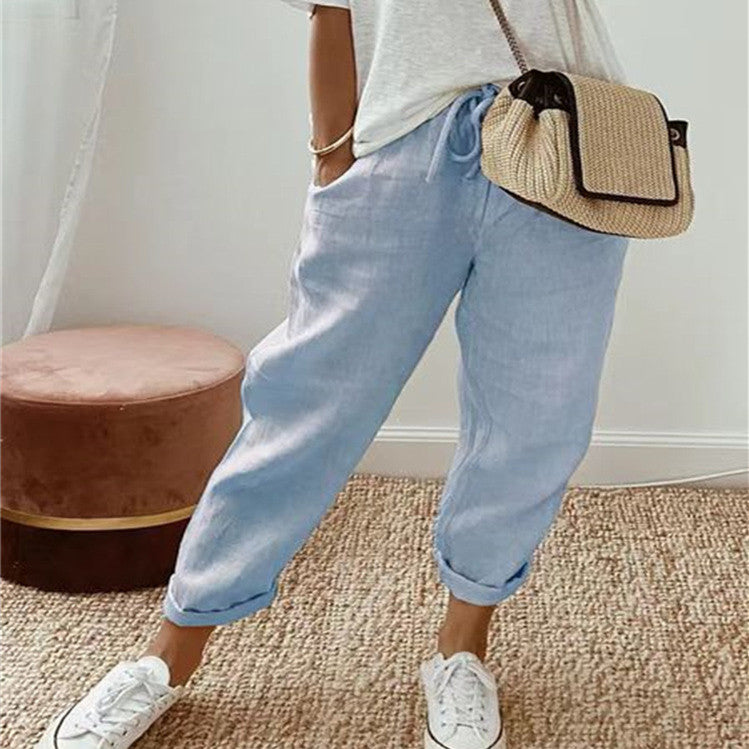 Person wearing light blue jeans and white sneakers with a straw bag, standing on a carpeted floor.