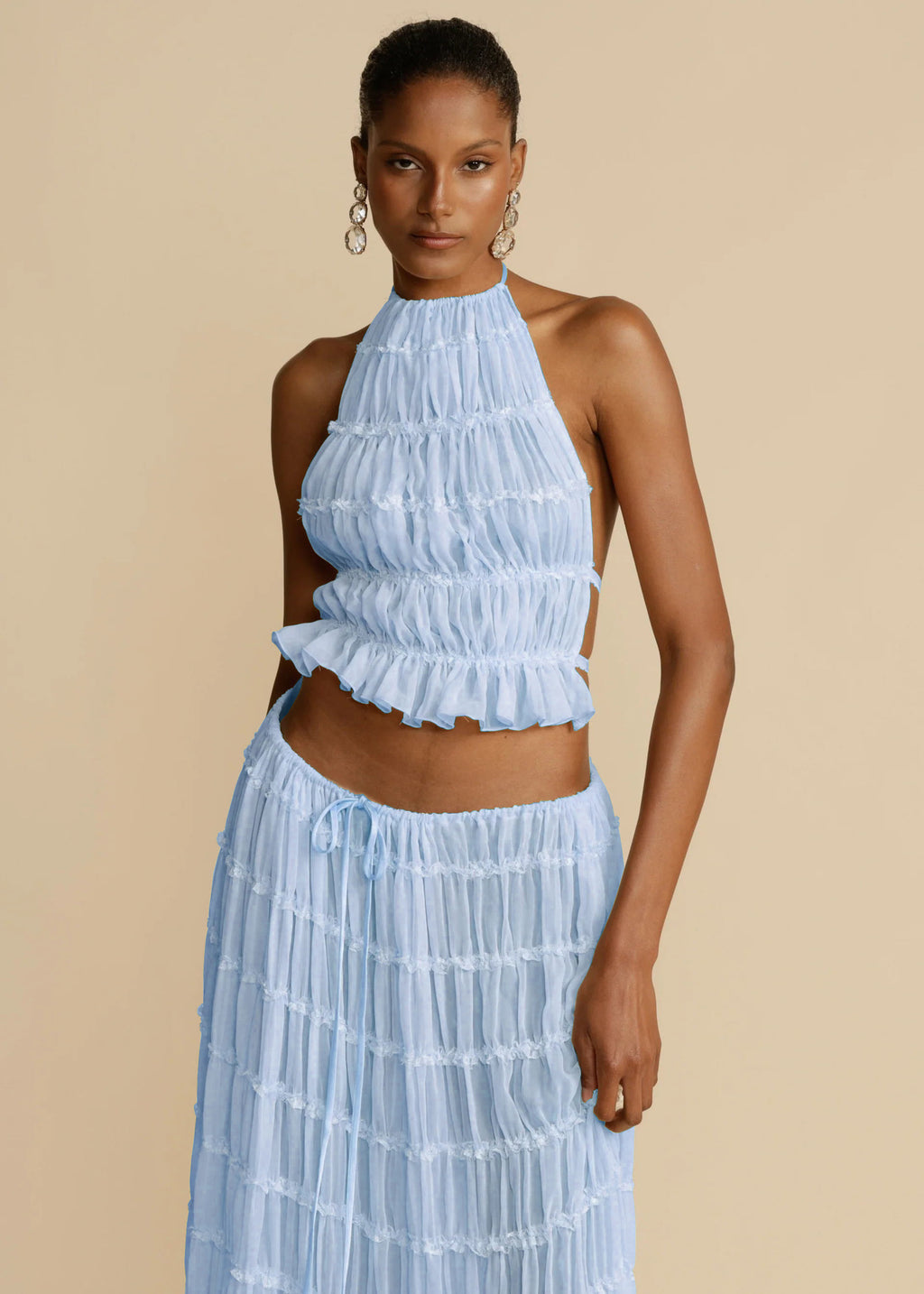 Woman wearing a light blue ruffled top and skirt set against a beige background