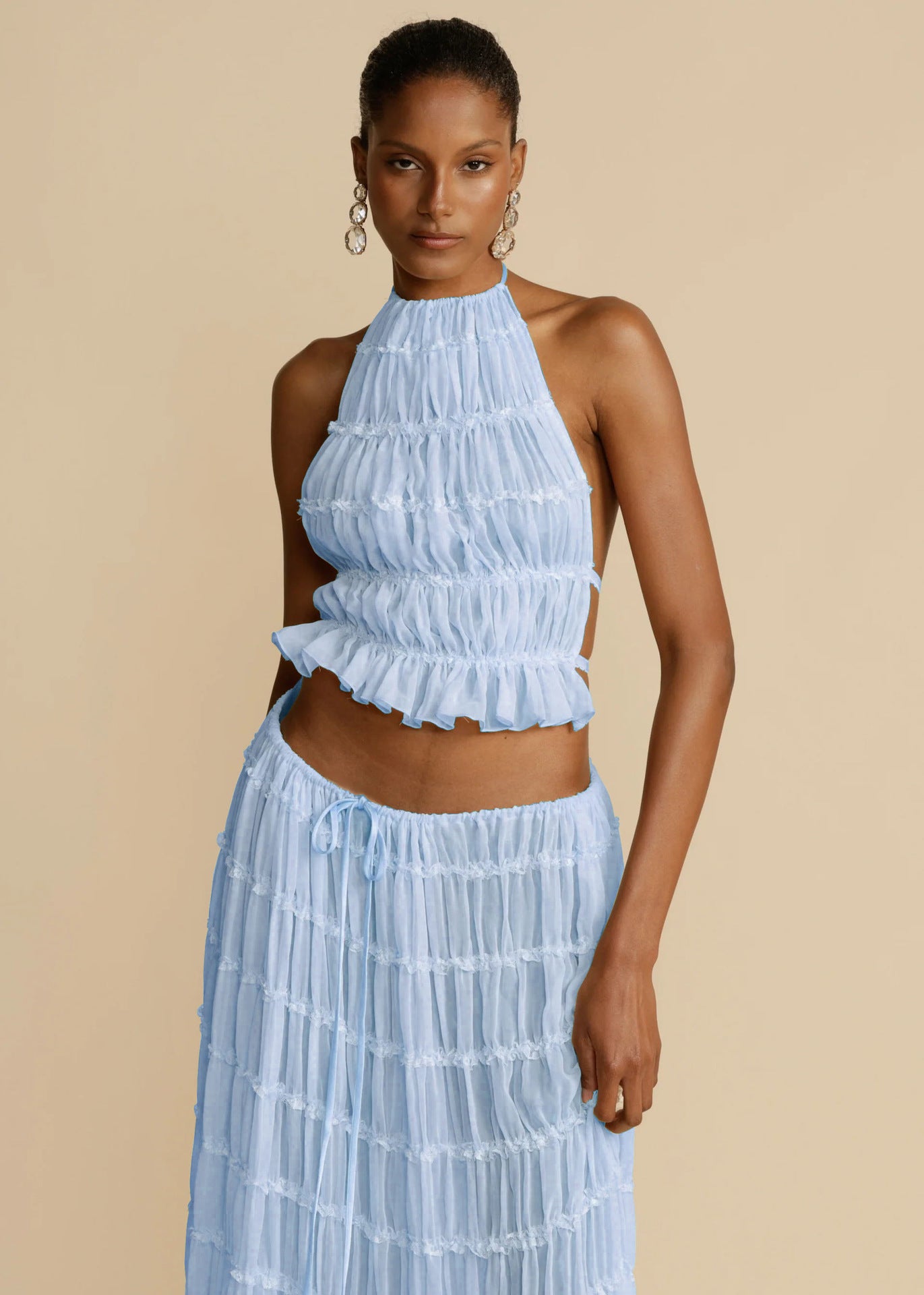 Woman wearing a light blue ruffled top and skirt set against a beige background