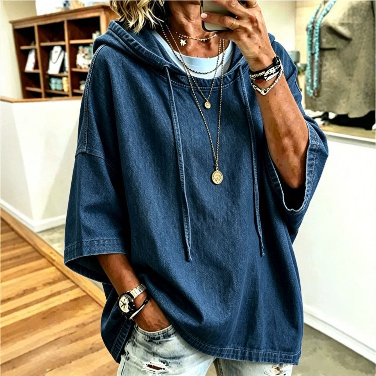 A woman takes a mirror selfie wearing an oversized dark blue denim hooded tunic top with wide three-quarter sleeves, layered over a light blue shirt and paired with distressed light-wash jeans.