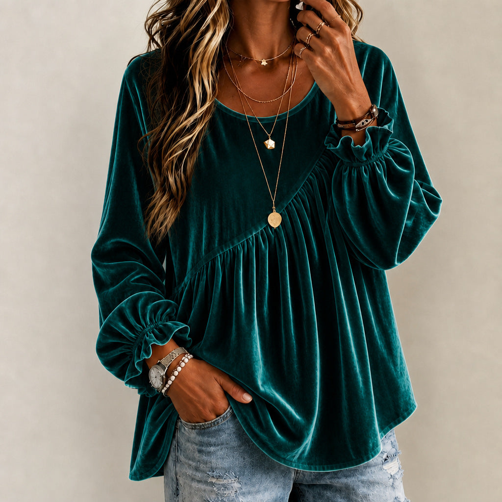 A woman wearing a long-sleeve velvet top in deep emerald green, paired with light-wash distressed denim jeans and layered gold necklaces, against a neutral beige background.