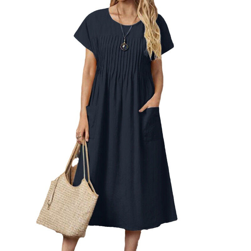 Woman wearing a navy blue dress with pockets holding a beige handbag on a white background