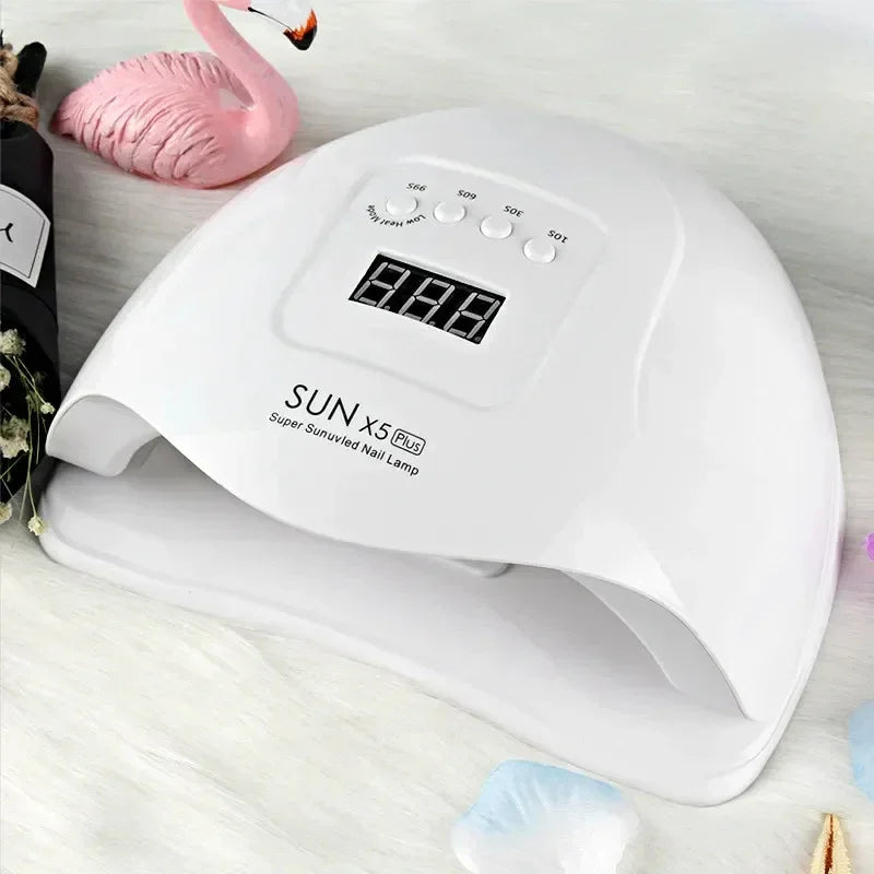 White SUN X5 Plus LED UV nail lamp with digital timer on tabletop, surrounded by decor.