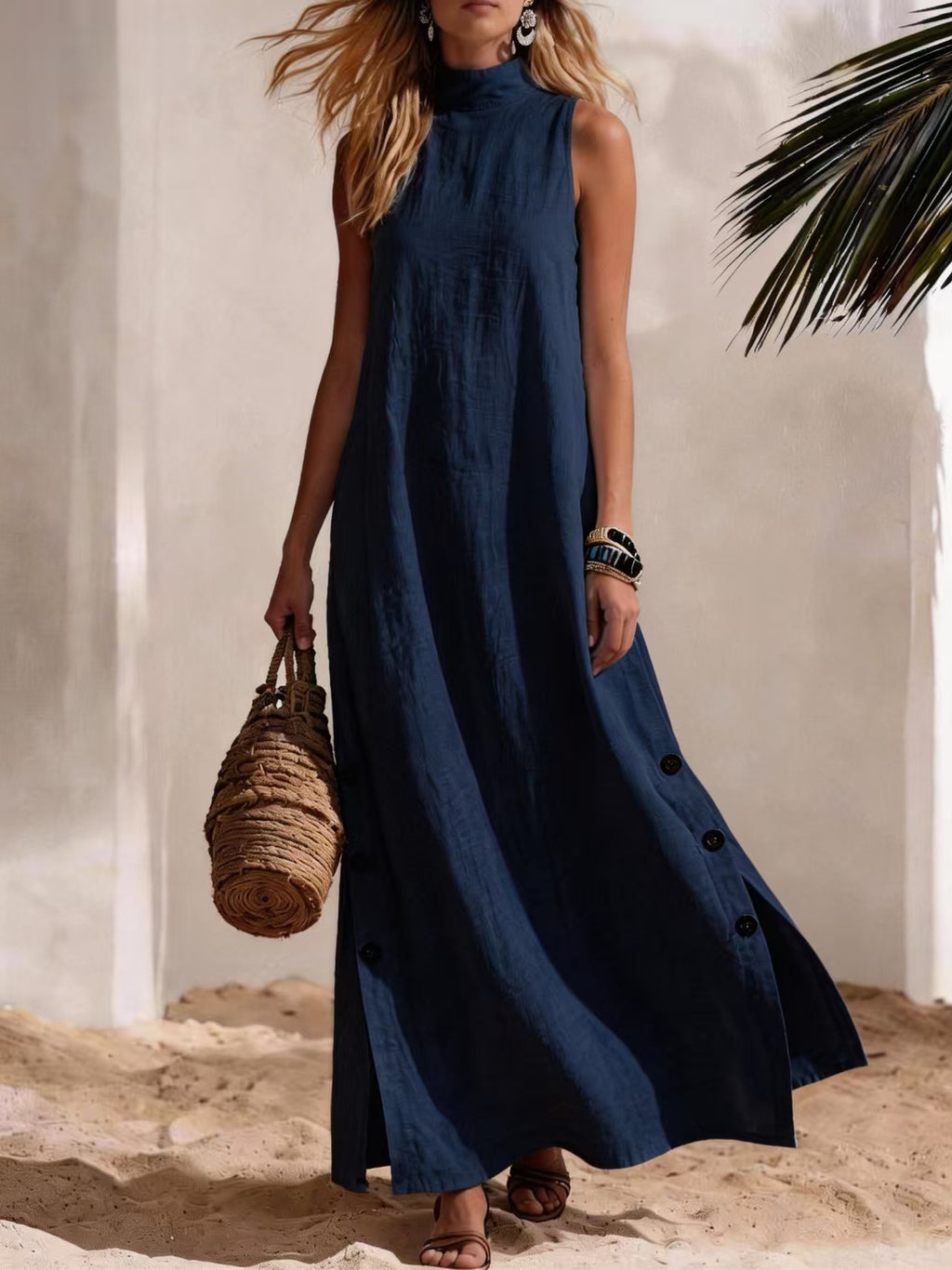 Woman wearing a long blue dress holding a woven bag on a sandy background