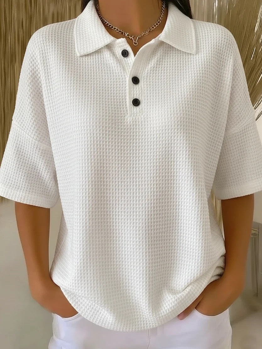 White textured polo shirt with black buttons worn by a person against a neutral background