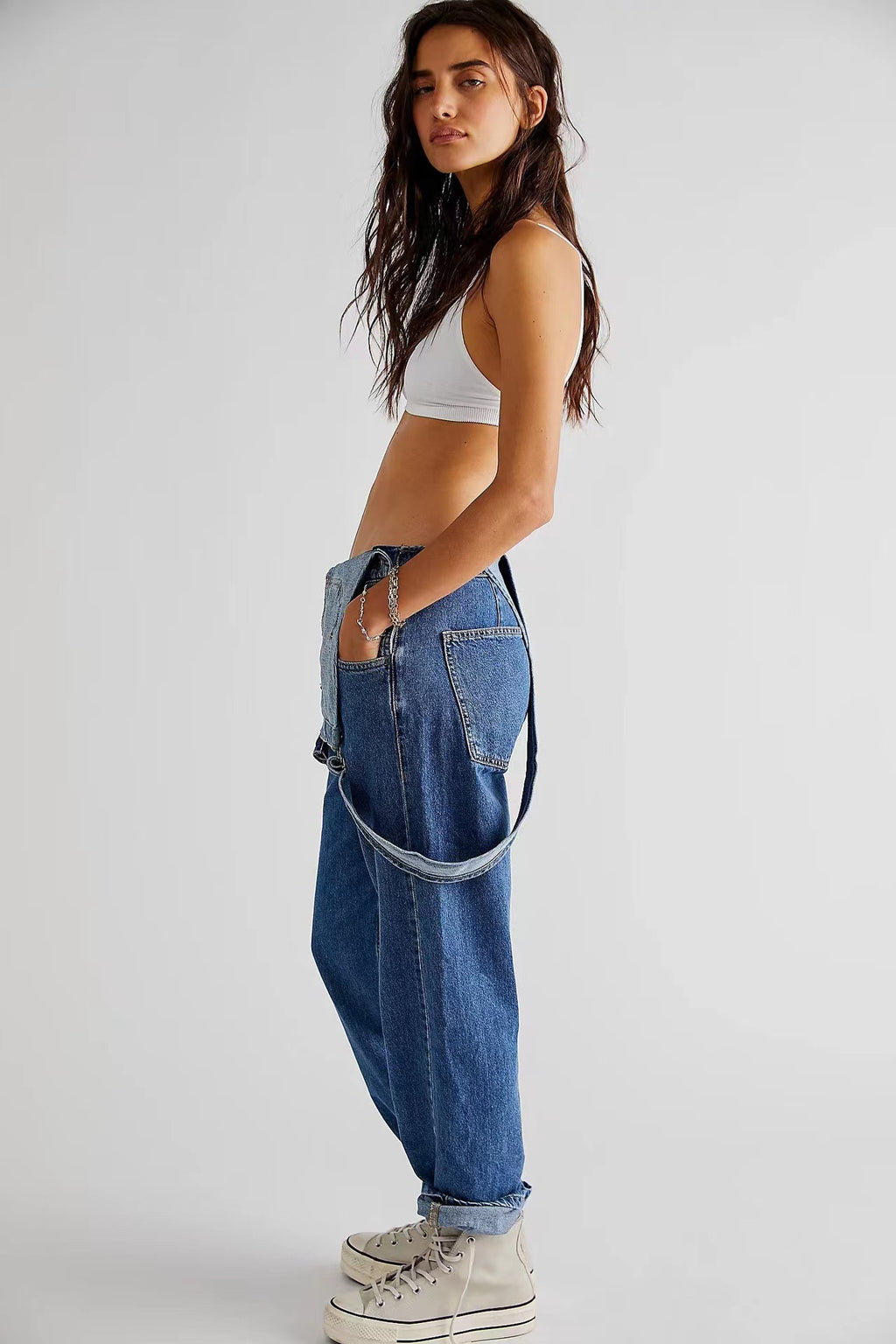 Woman wearing a white crop top and blue jeans on a plain background