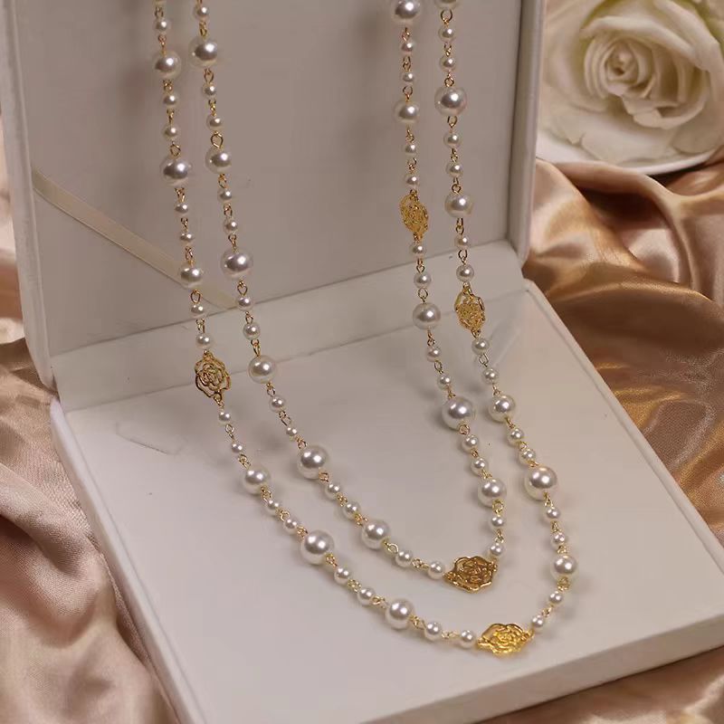 Pearl necklace with gold accents on a white box with a rose in the background