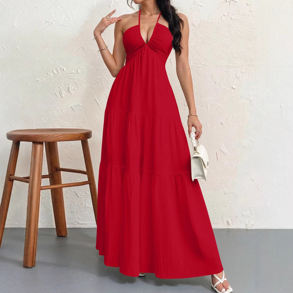 Woman wearing a red halter neck dress holding a white clutch against a white wall.