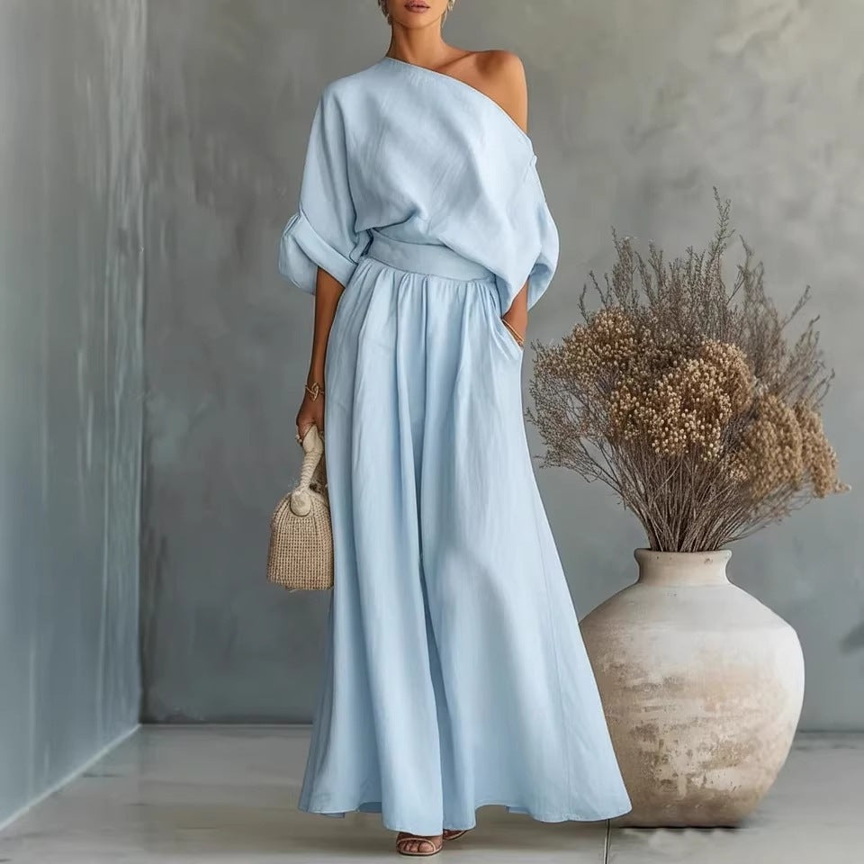 Woman wearing a light blue dress standing next to a textured wall and decorative vase.
