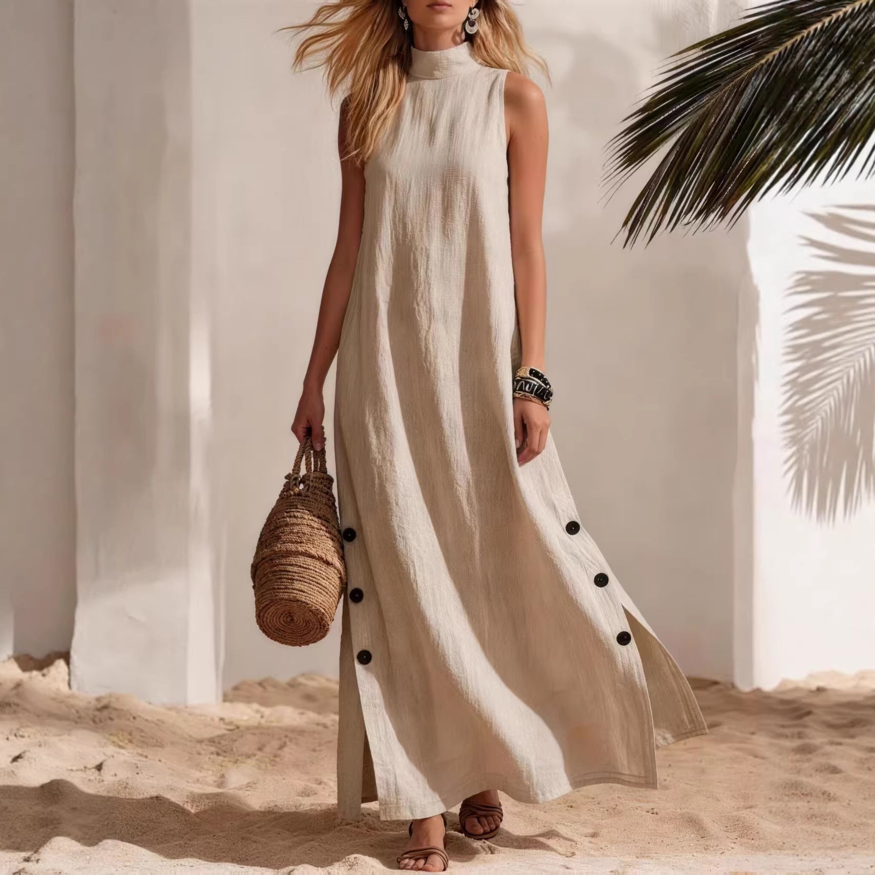 Woman in a long white dress with black buttons standing on sand with palm leaves in the background