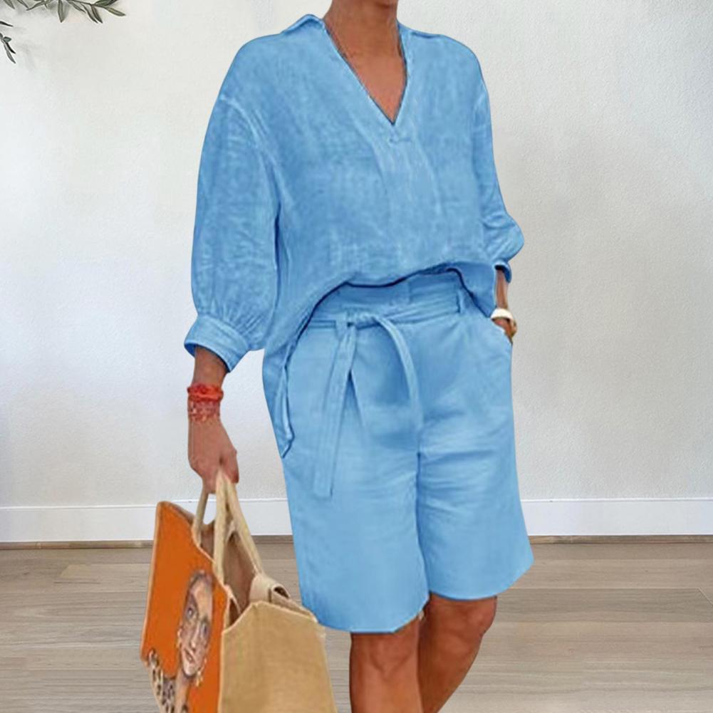 Person wearing a blue outfit with shorts and a top, holding two bags indoors.