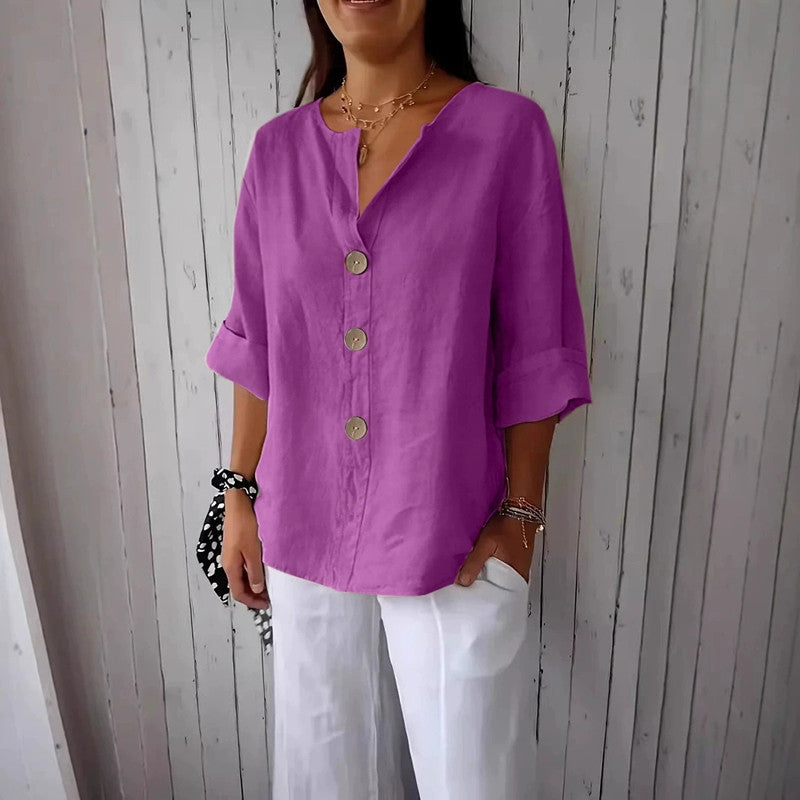 Person wearing a purple button-up shirt and white pants against a wooden paneled wall.