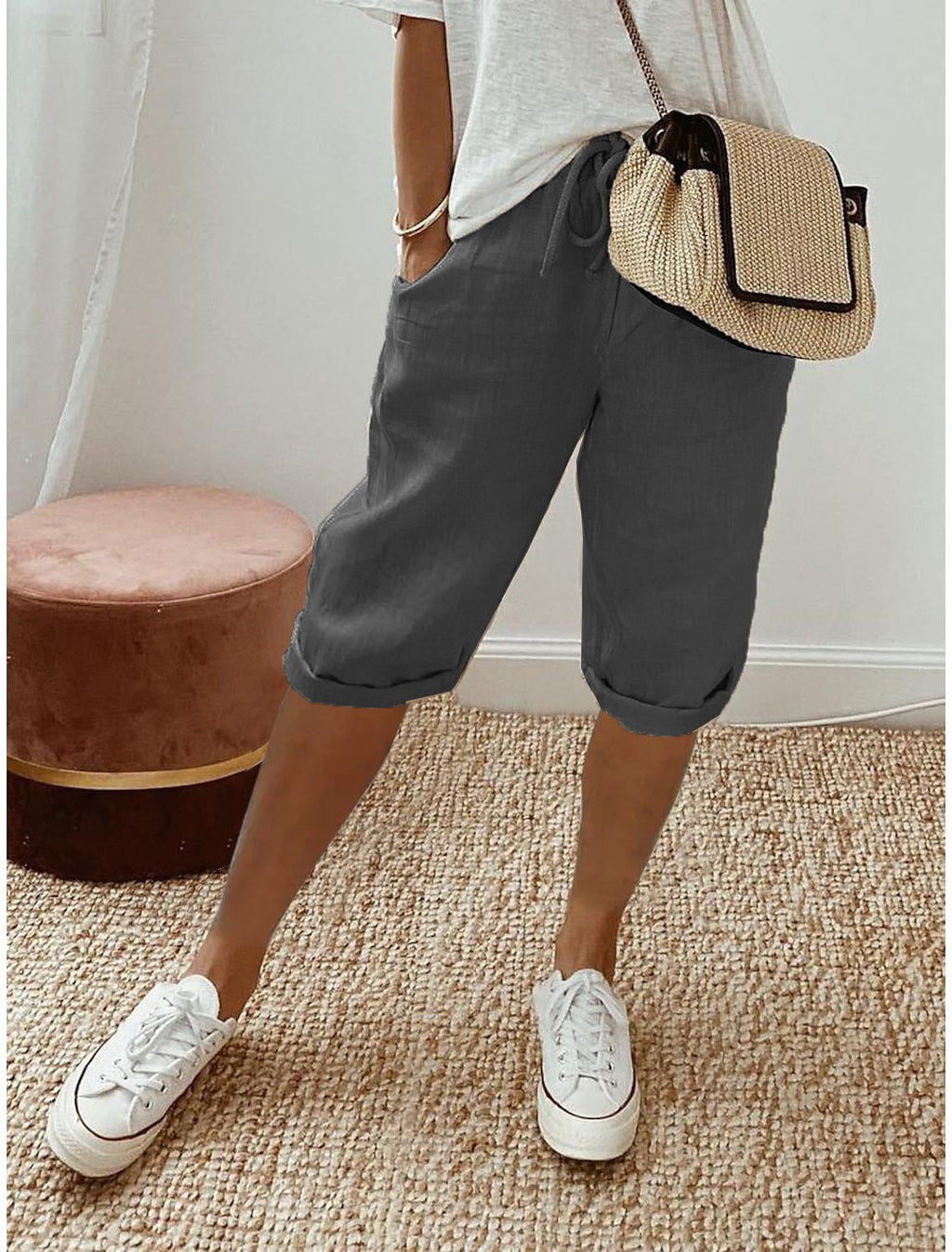 Person wearing gray shorts, white sneakers, and a beige bag on a neutral background