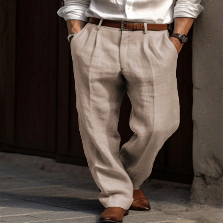 Person wearing beige pleated pants and a white shirt with a brown belt and shoes, standing against a dark wall.