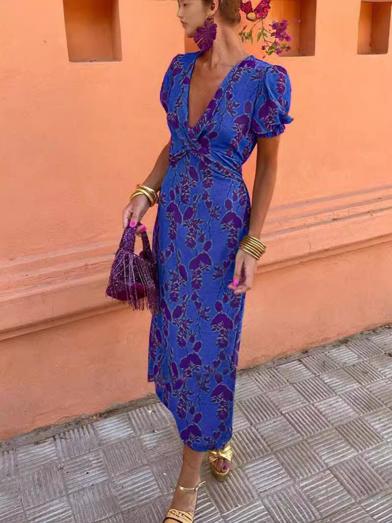 Woman in a blue floral dress standing against an orange wall.