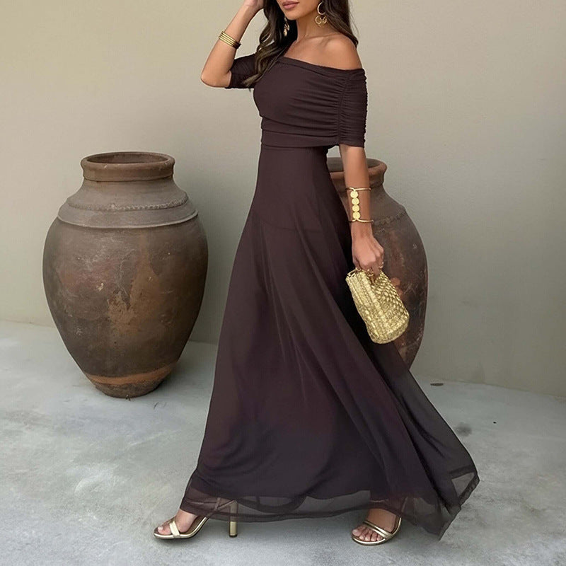Woman in a brown off-shoulder dress holding a gold clutch against a neutral background