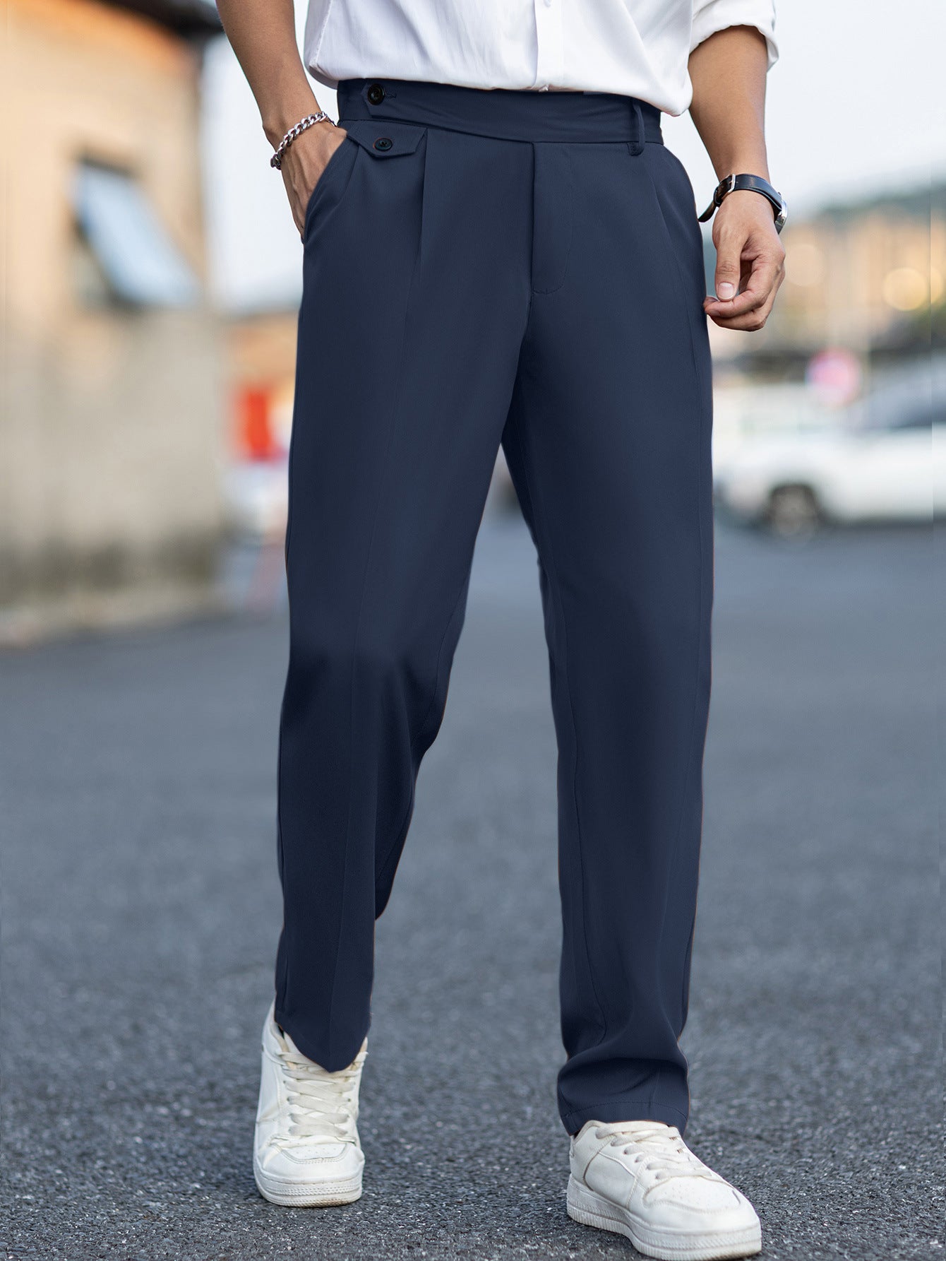 Person wearing navy pants and white sneakers on a blurred street background