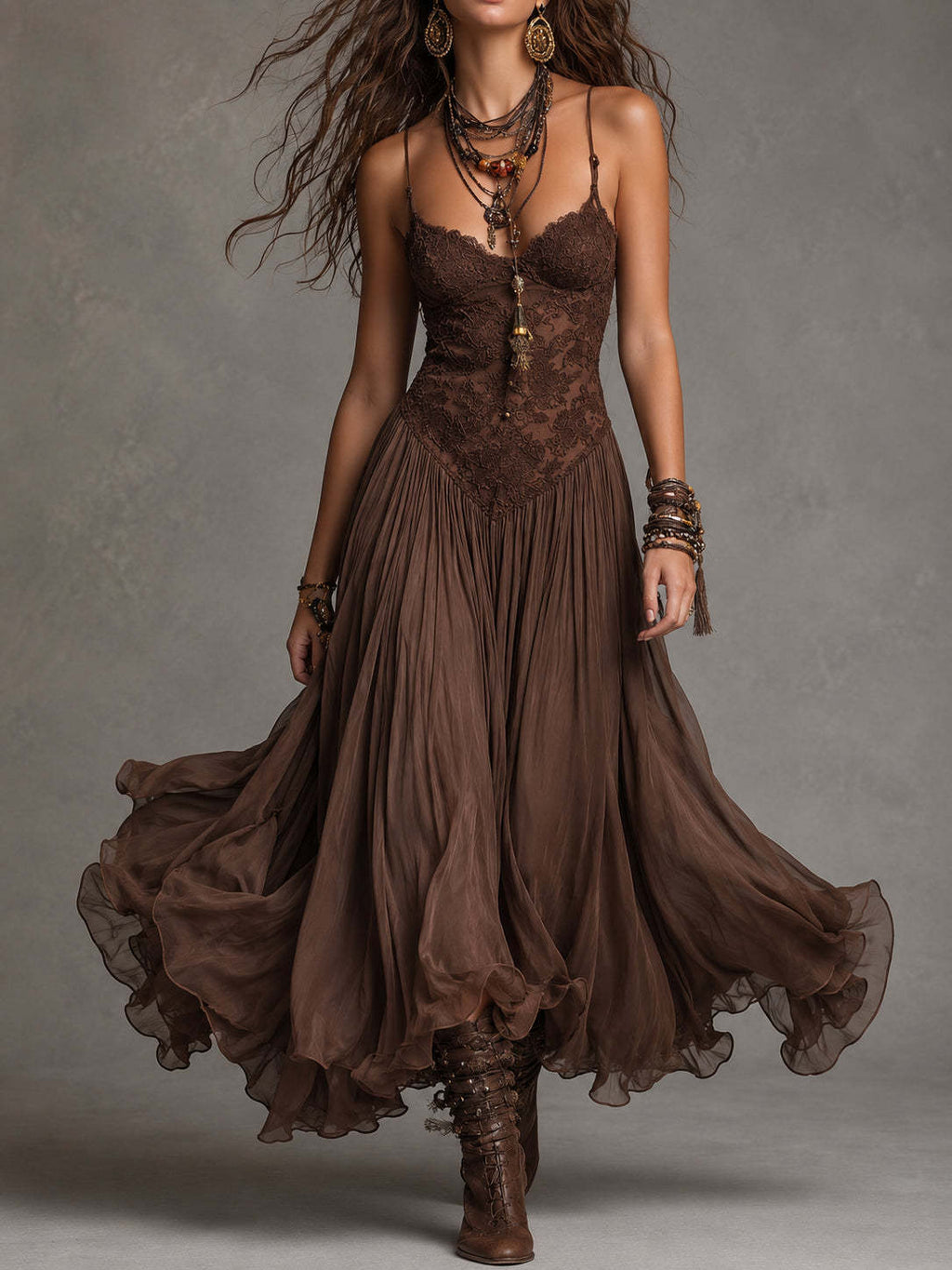 A woman modeling a brown bohemian-style midi dress with a lace corset bodice, spaghetti straps, and a flowing chiffon skirt, paired with brown lace-up boots against a textured gray studio background.