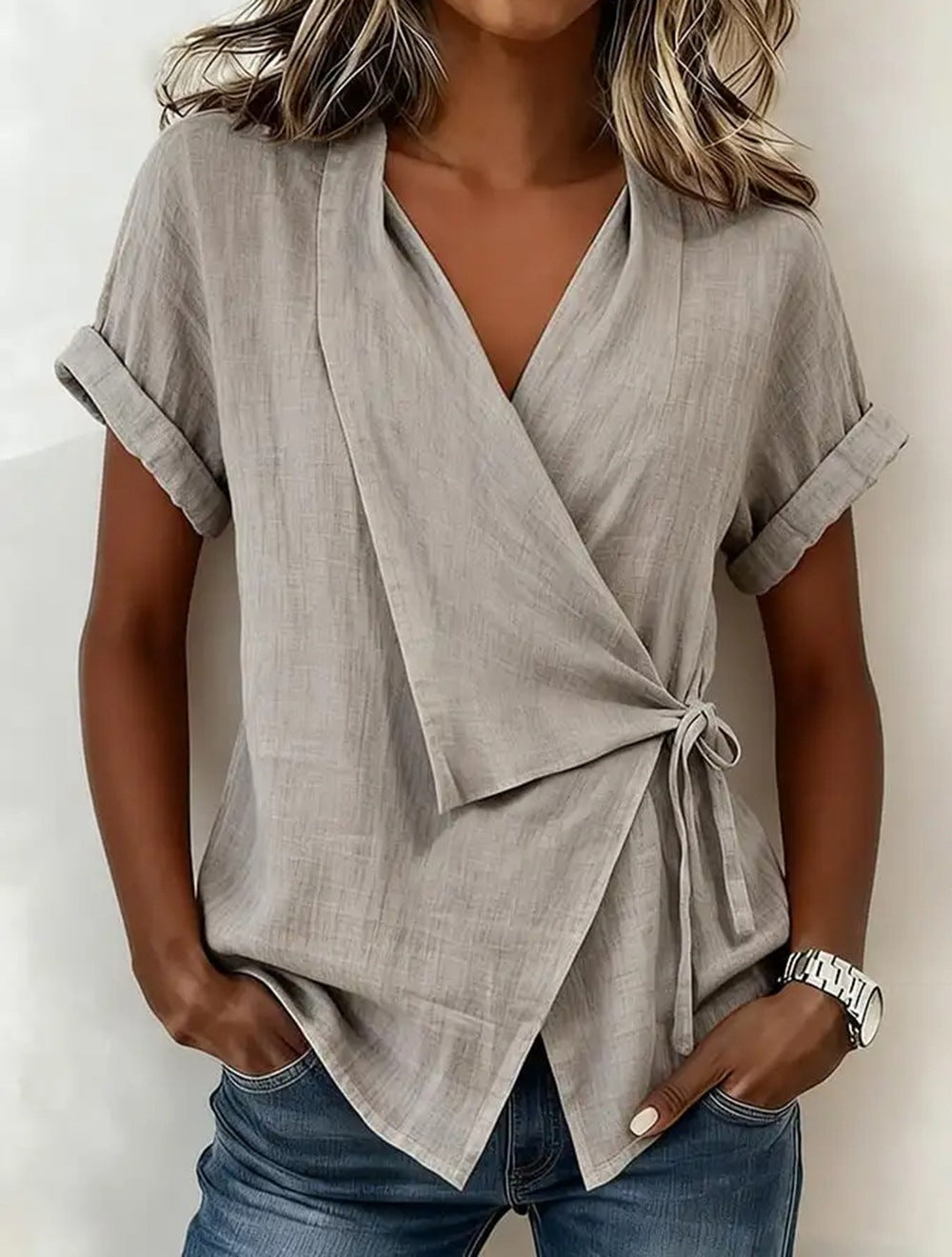 Woman wearing a light gray wrap top with short sleeves and blue jeans on a white background