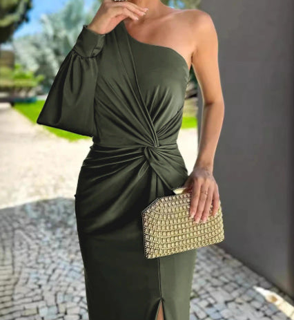 Woman wearing a green one-shoulder dress holding a gold clutch outdoors.