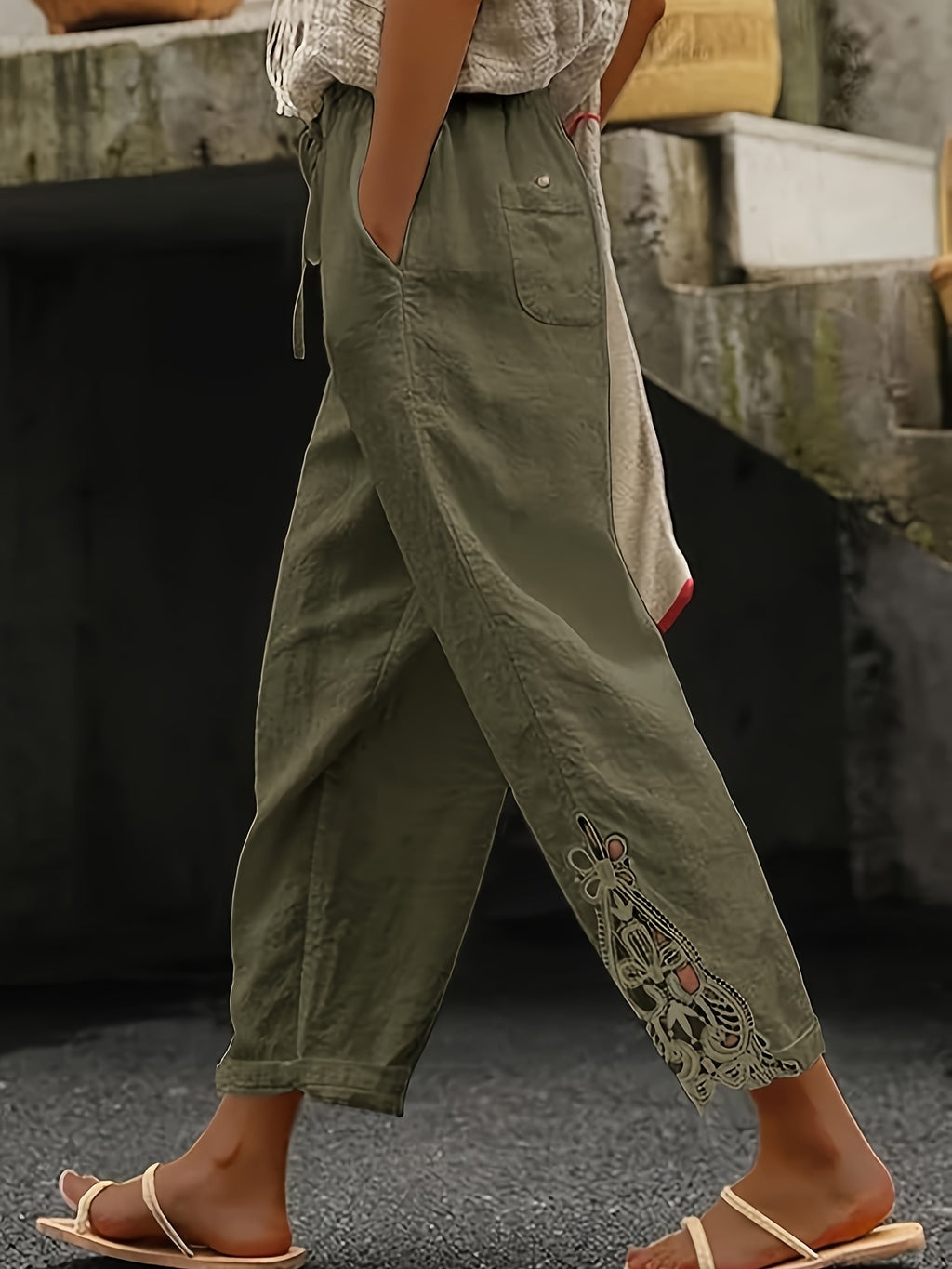 Person wearing green pants with lace details and a white top, standing on a stone surface.