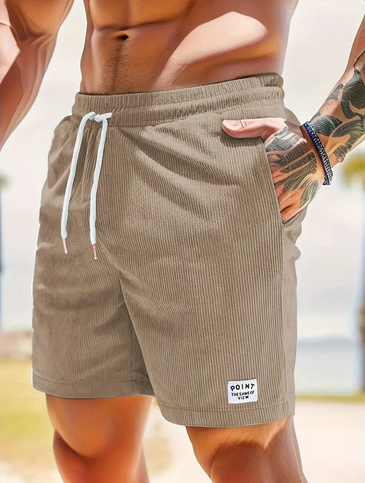Beige shorts with a brand label worn by a person on a blurred beach background
