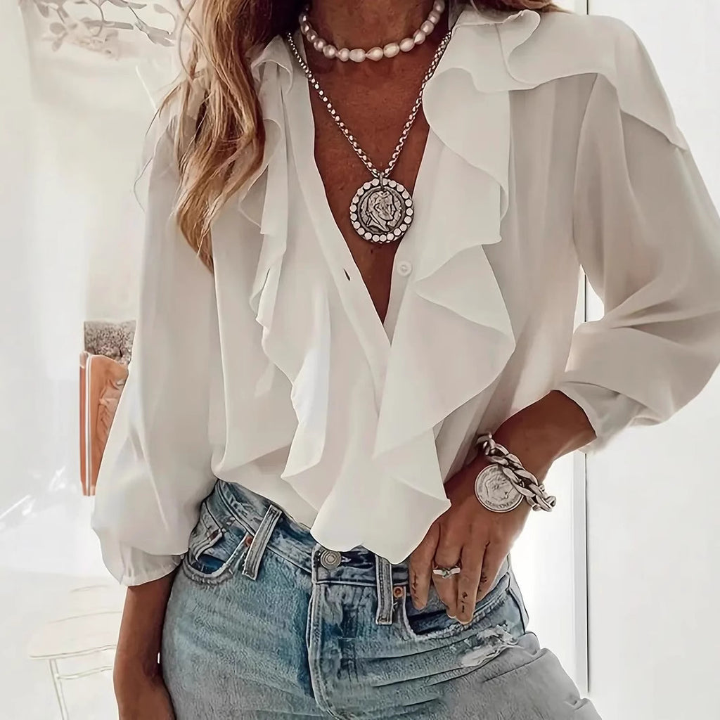 Person wearing a white blouse with ruffled details, pearl necklace, and denim jeans.