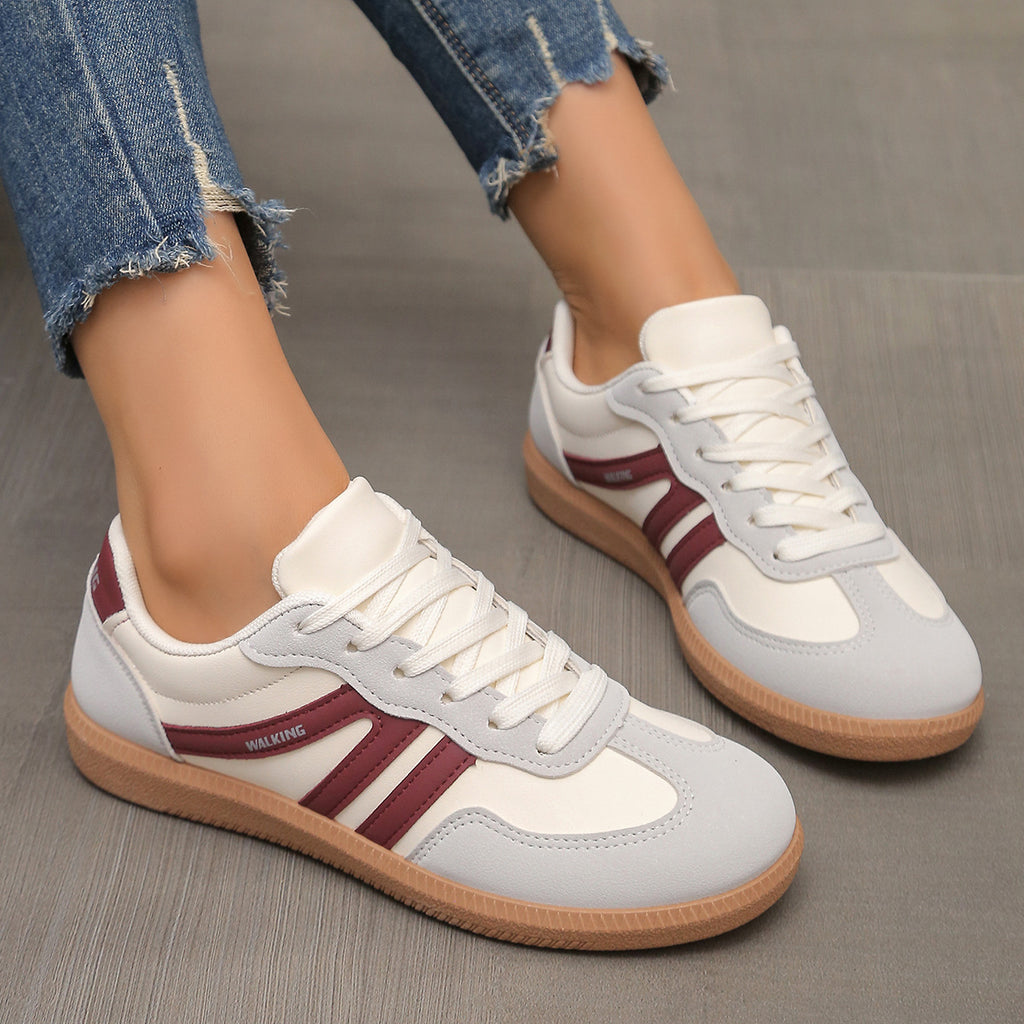 White and gray sneakers with red accents worn with blue jeans on a neutral background