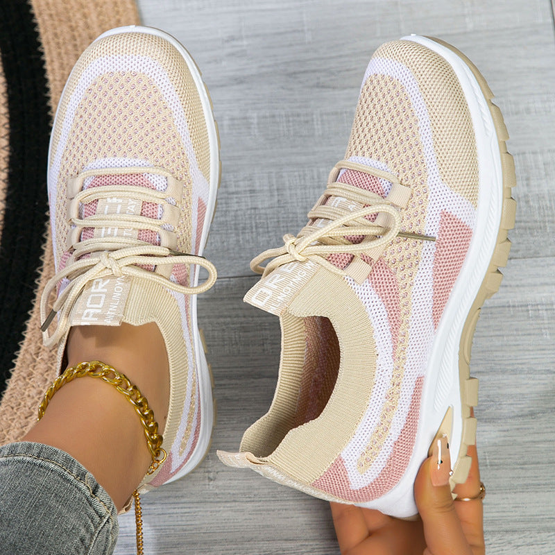 Beige sneakers with white soles worn by a person on a wooden floor.