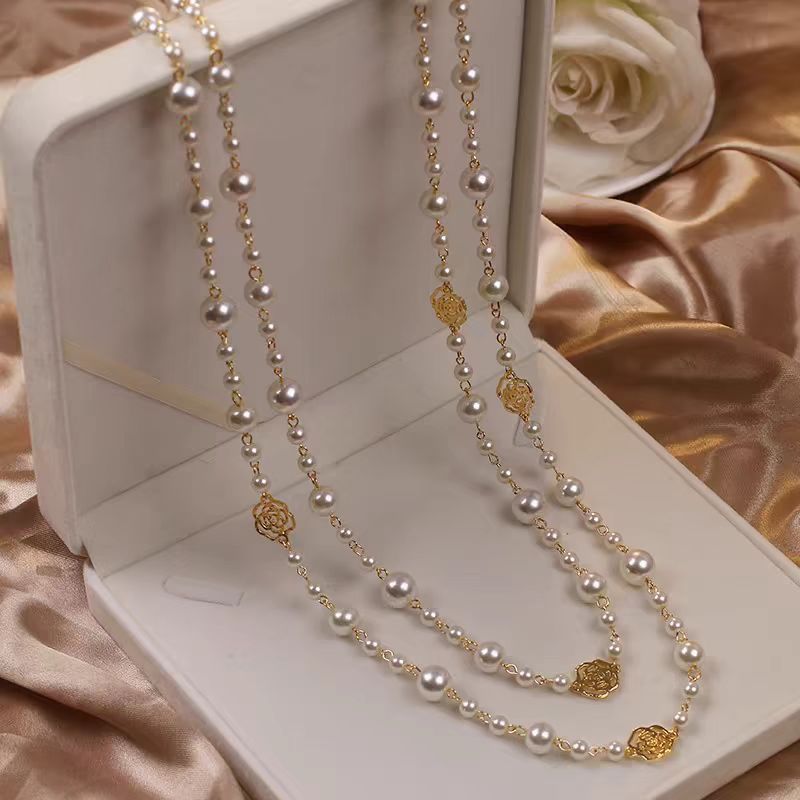 Pearl necklace with gold accents on a white box with flowers in the background
