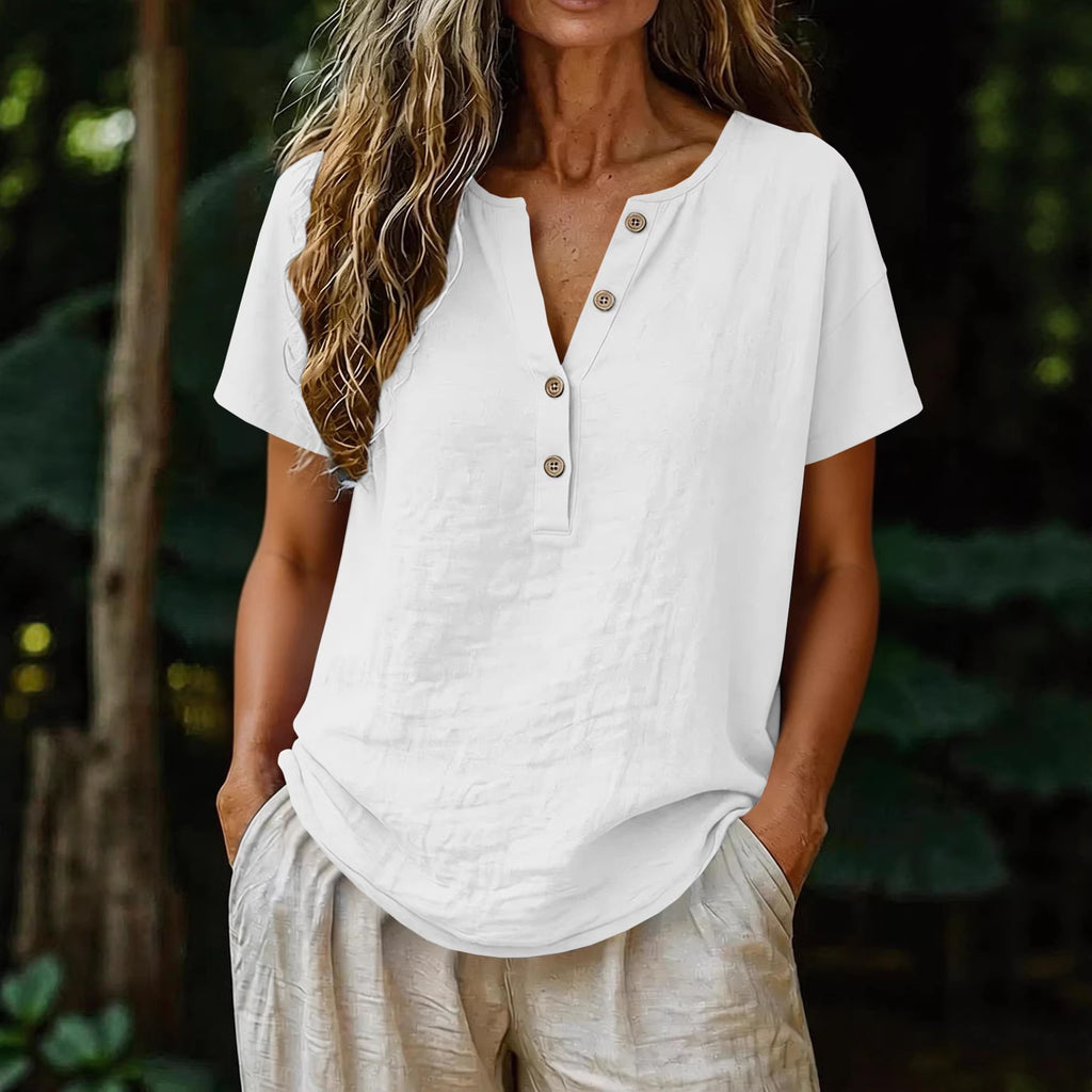 Woman wearing a white button-up shirt and beige pants with a blurred natural background
