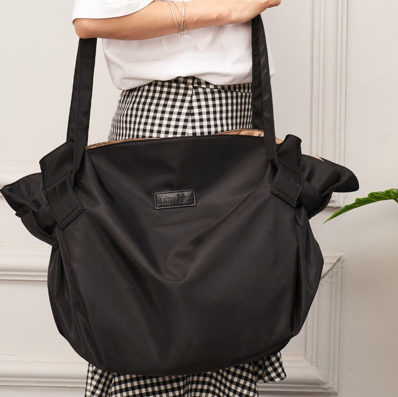 Person holding a black shoulder bag with a visible brand label against a neutral background
