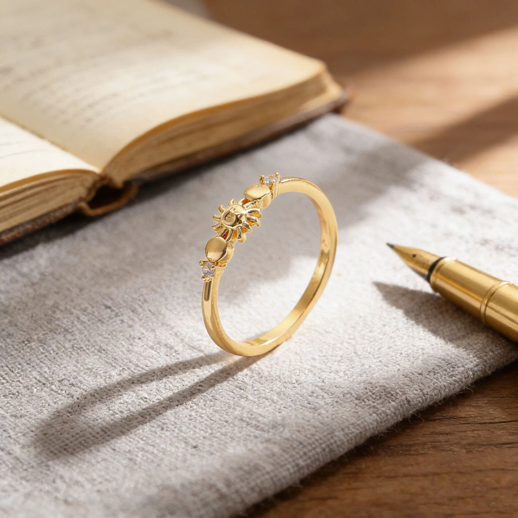 Gold ring with star and moon design on a textured surface with an open book and pen.
